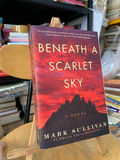 Beneath a Scarlet Sky novel by Mark Sullivan, displayed on wooden stand amid bookshelves